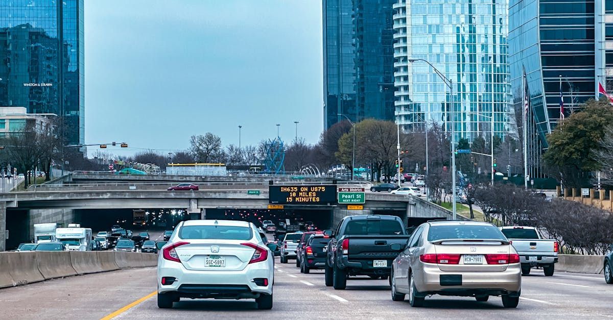 A row of cars are driving down a highway in a city.