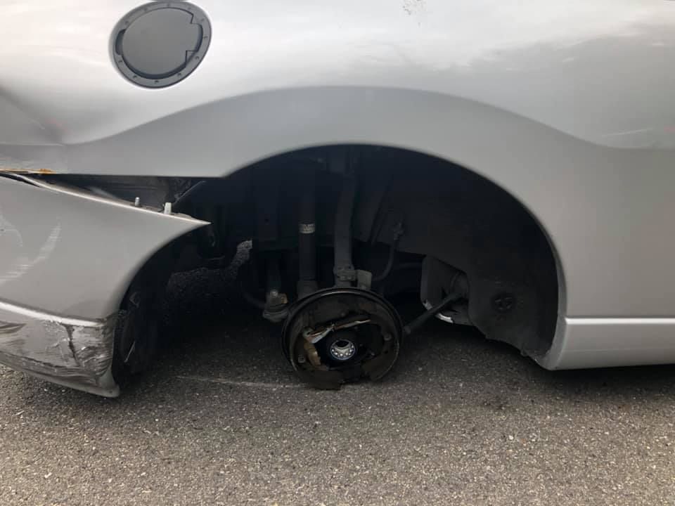 A silver car with a broken wheel is parked on the side of the road.