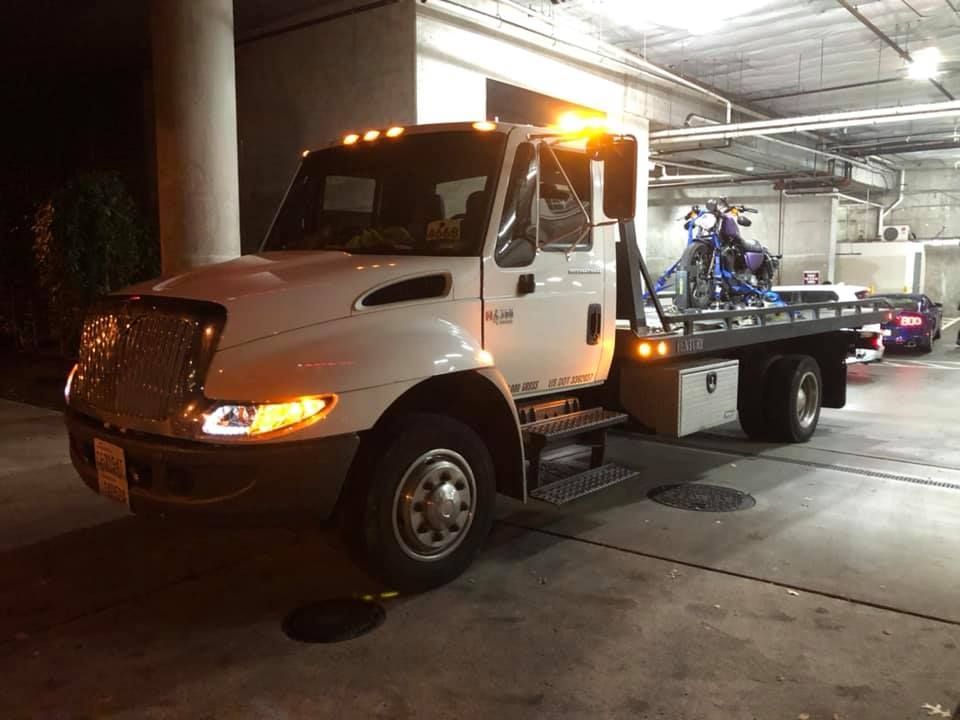 A tow truck with a motorcycle on the back is parked in a parking garage.