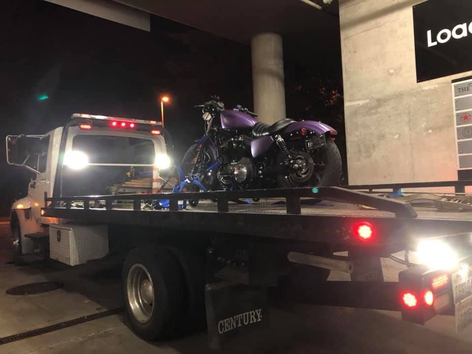 A purple motorcycle is on the back of a tow truck.