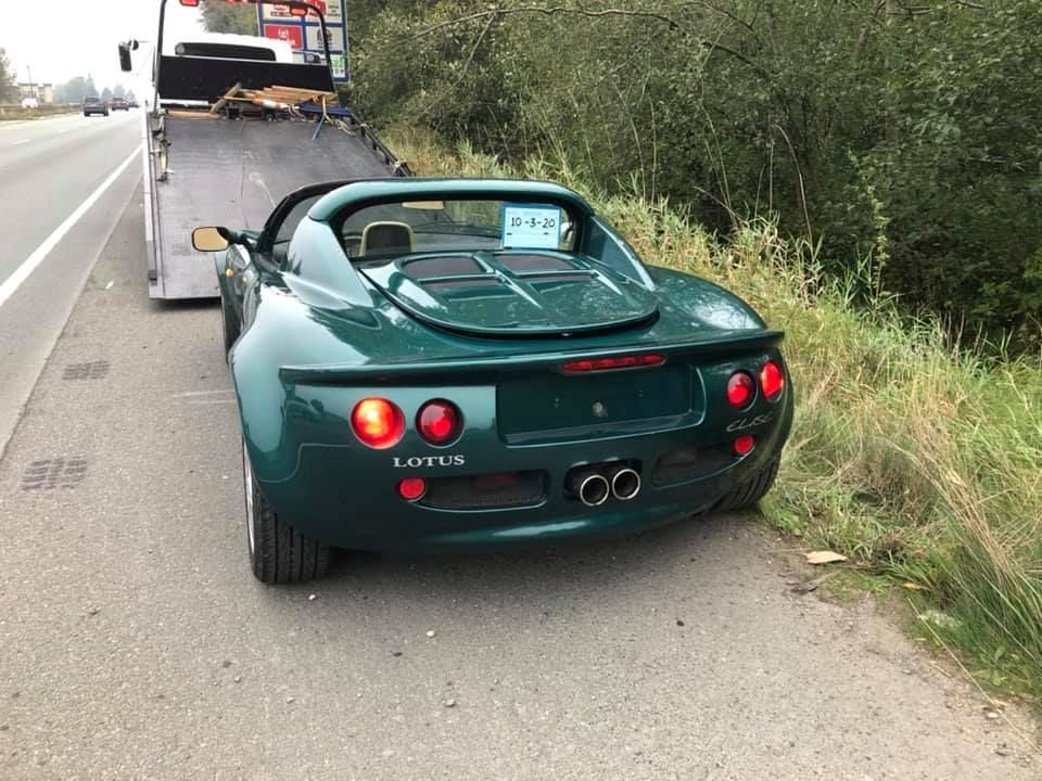 A green lotus sports car is being towed down the road by a tow truck.