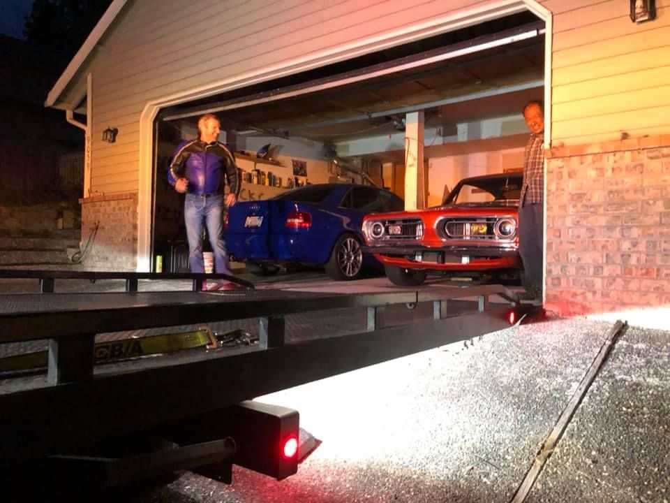 Two cars are parked in a garage with a tow truck behind them