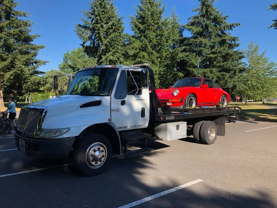 A tow truck is carrying a red car on the back of it.