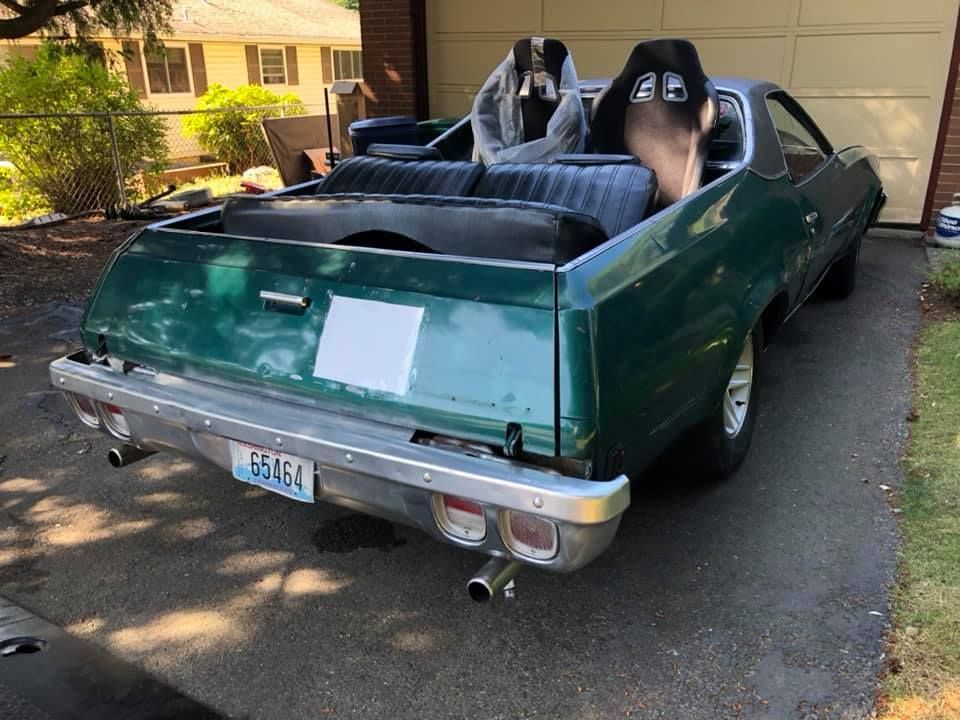 A green car with two seats in the back is parked in a driveway.