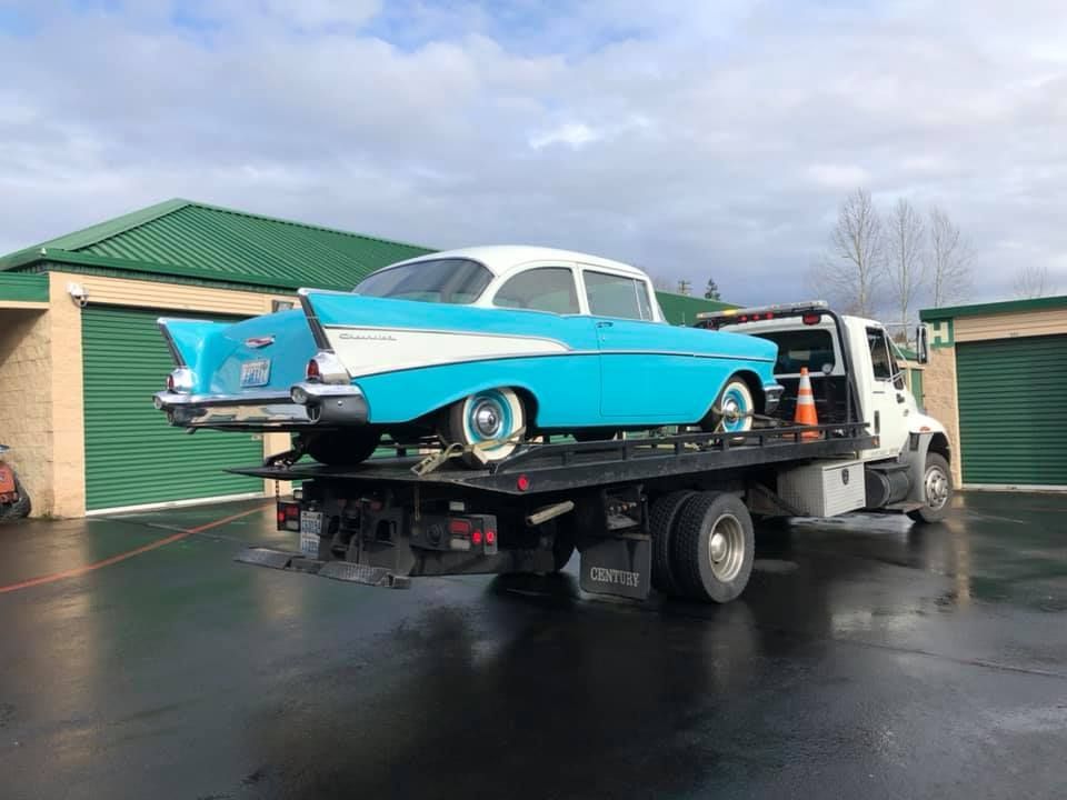 A blue and white car is being towed by a tow truck.