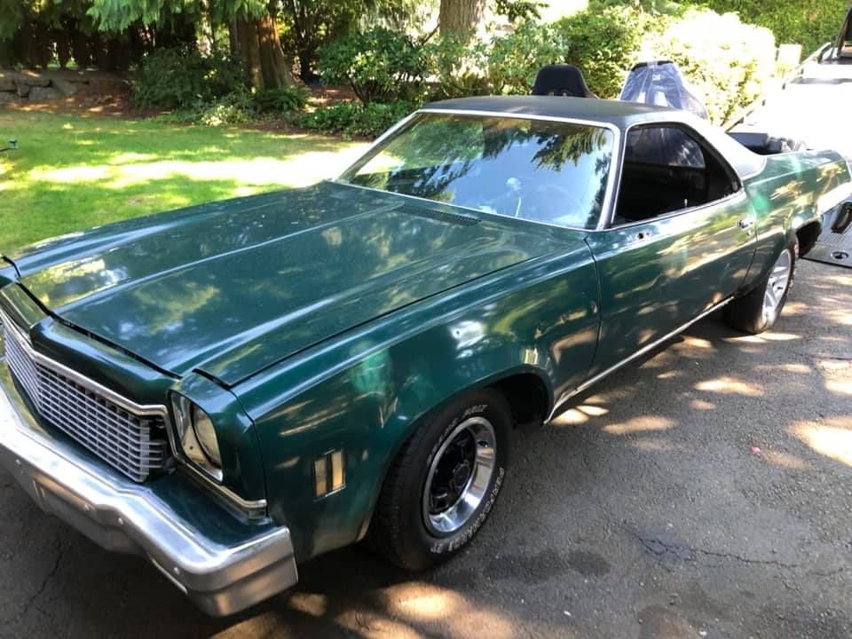 A green car is parked in a driveway with trees in the background