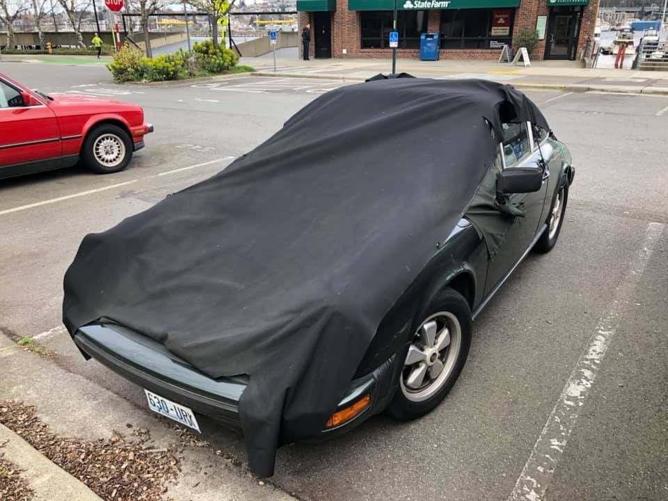 A black car with a black cover on it is parked on the side of the road