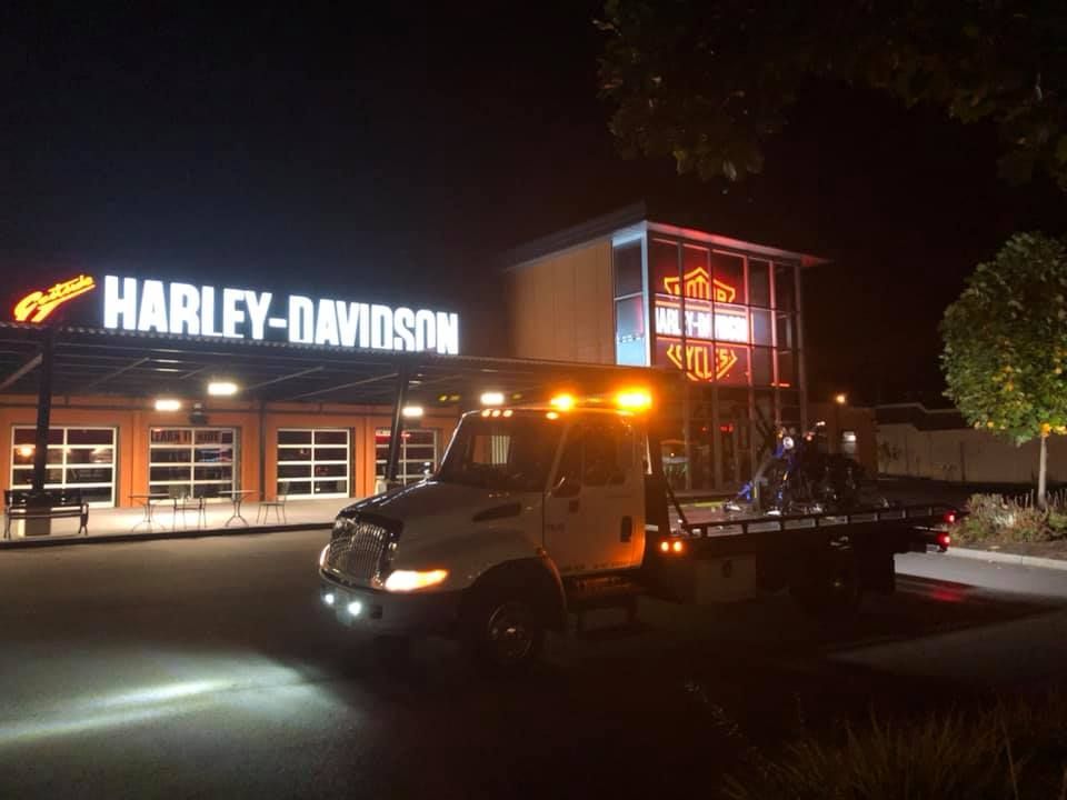 A tow truck is parked in front of a harley davidson store at night.