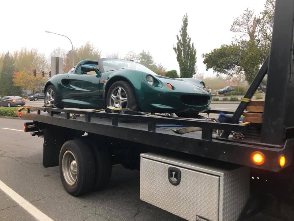 A green sports car is being towed by a tow truck.