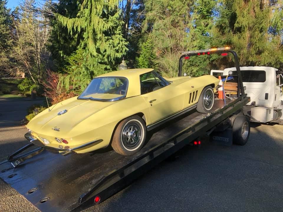 A yellow corvette is being towed by a tow truck.