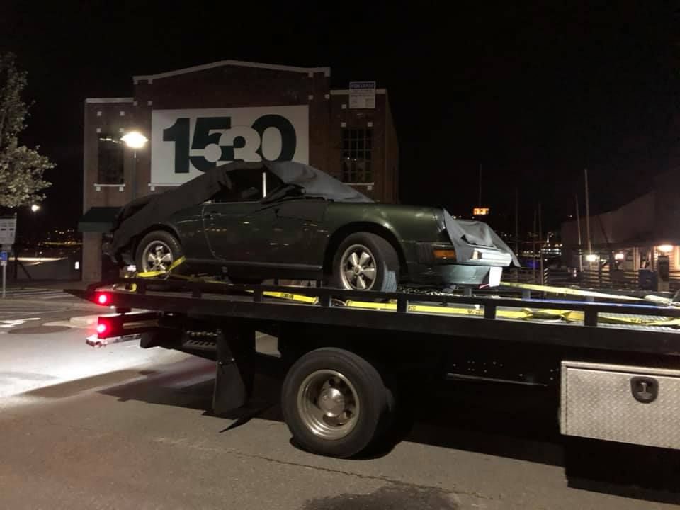 A car is being towed by a tow truck in front of a building with the number 15 on it