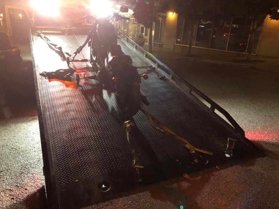 A motorcycle is being towed by a tow truck at night.