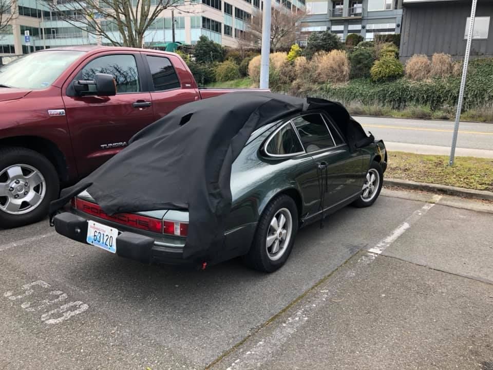A green car is parked in a parking lot next to a red truck.