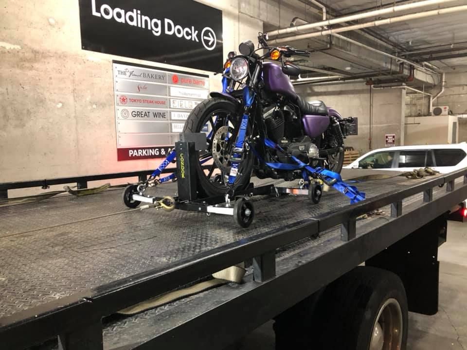 A purple motorcycle is sitting on top of a tow truck.