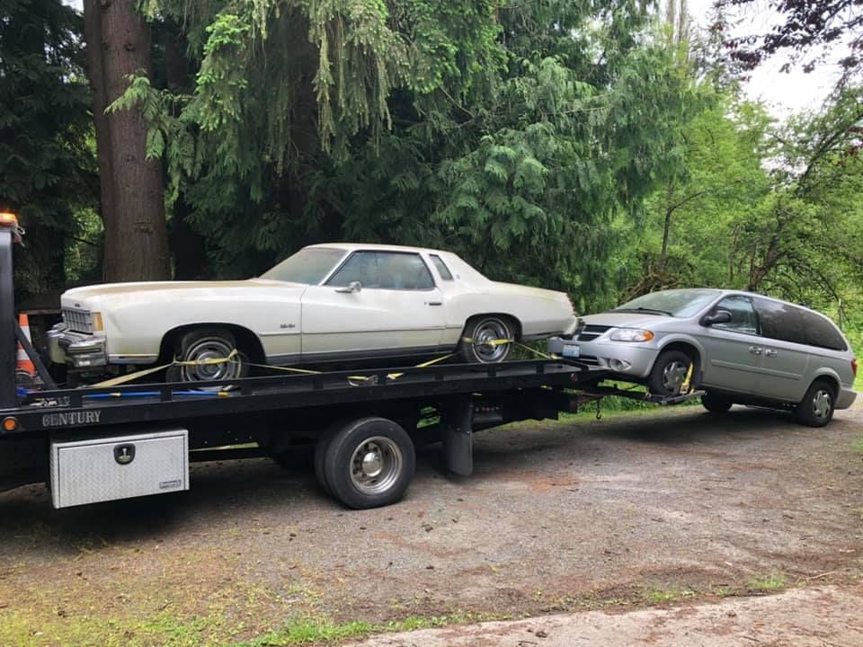 A white car is being towed by a tow truck.