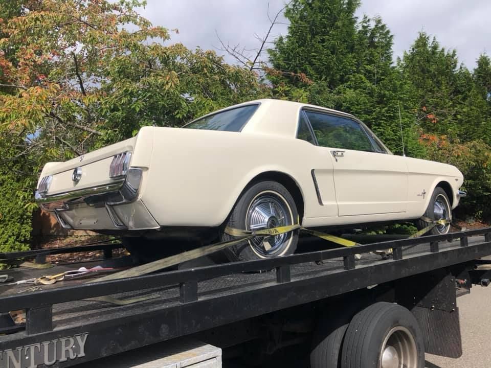 A white mustang is being towed by a tow truck.