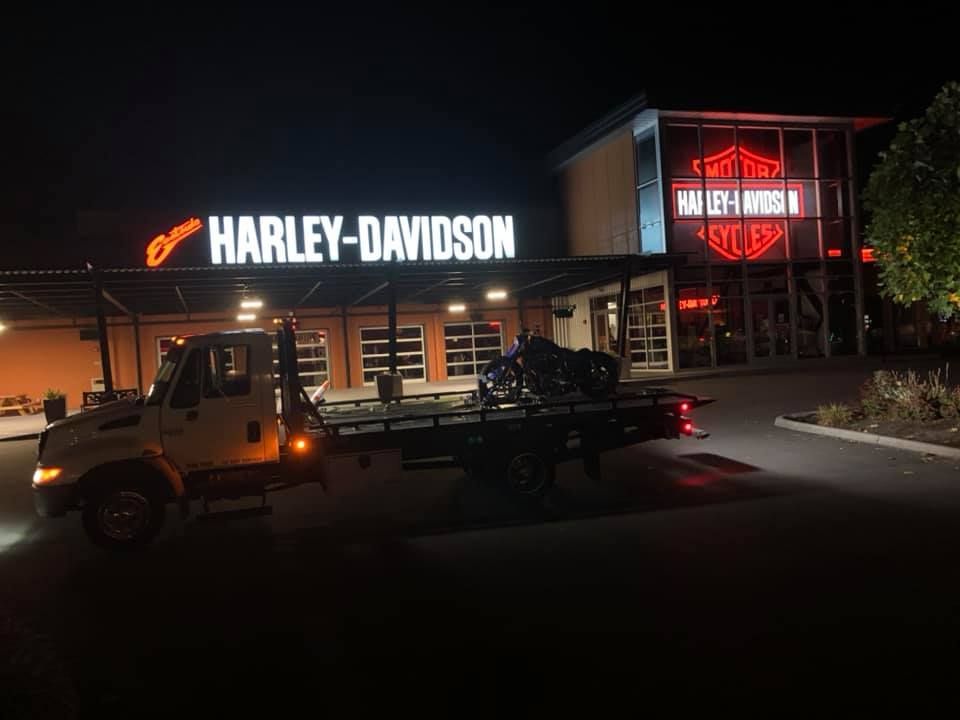 A tow truck is towing a motorcycle in front of a harley-davidson store.