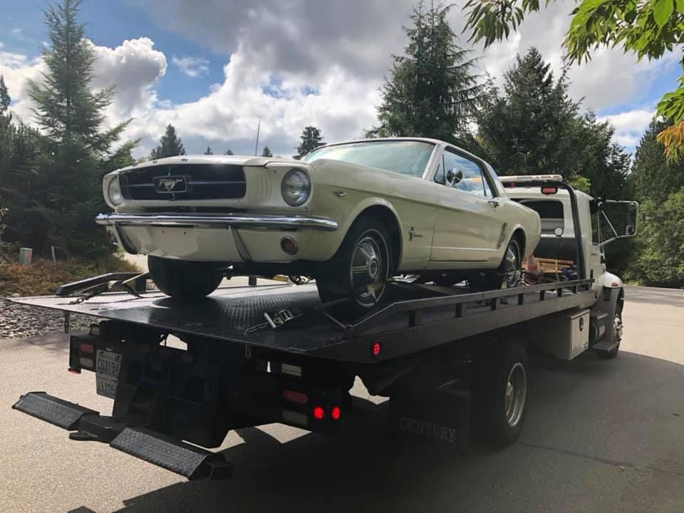 A white mustang is sitting on top of a tow truck.