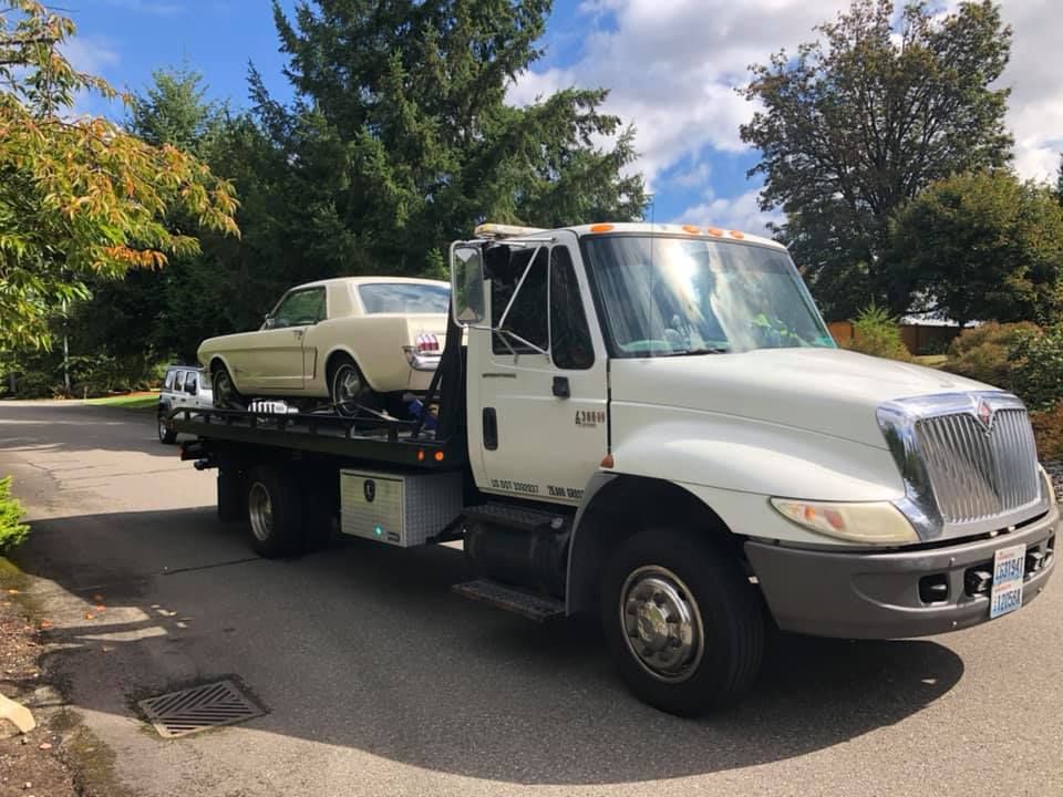 A white tow truck is carrying a white car on the back.