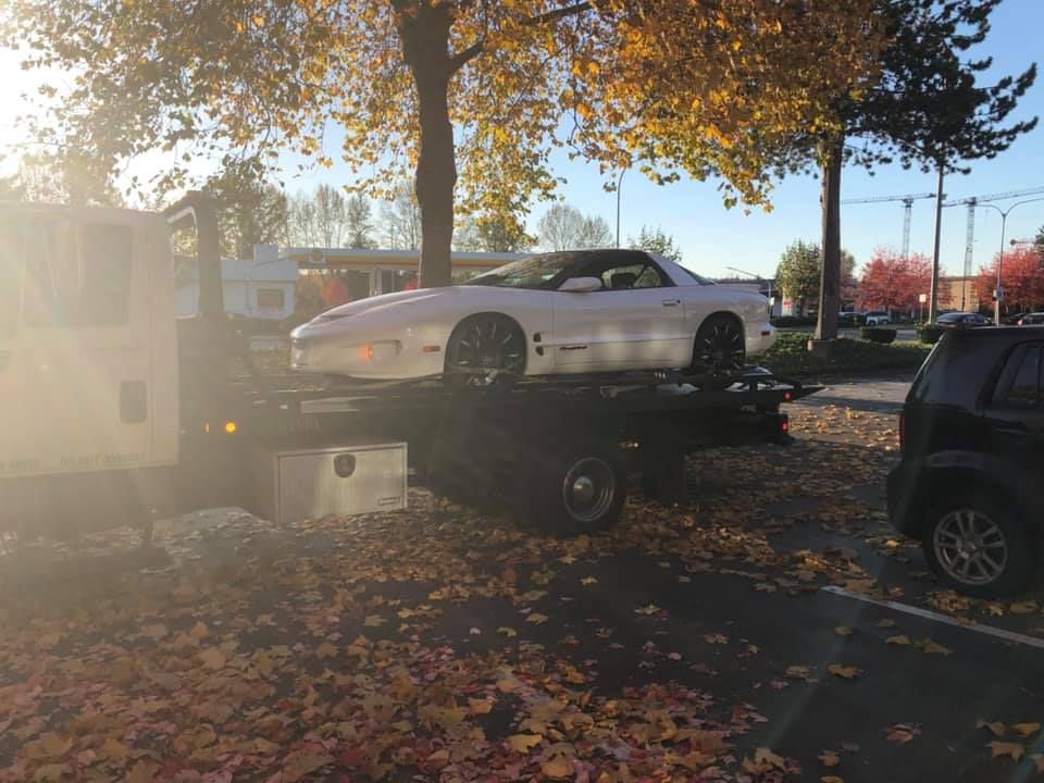 A white car is being towed by a tow truck.