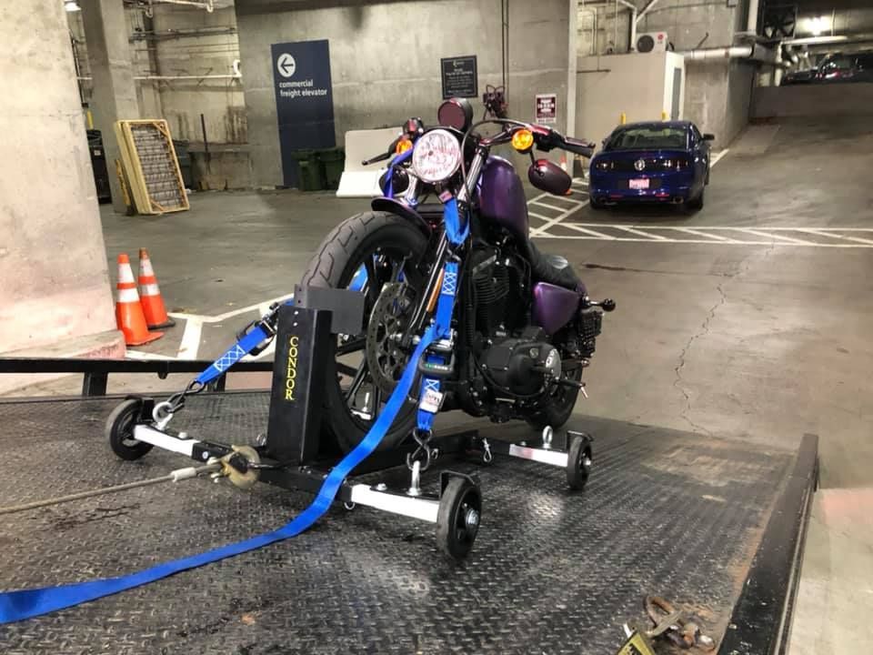 A purple motorcycle is sitting on a tow truck in a parking garage.