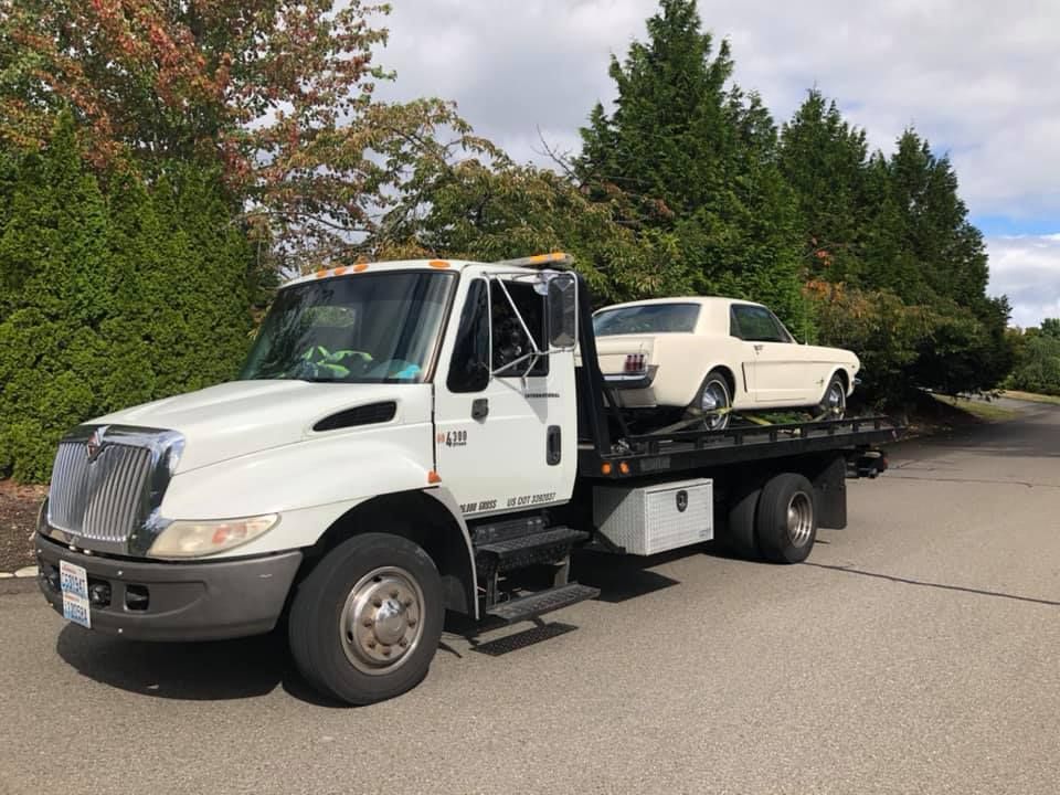 A white tow truck is carrying a white mustang on the back of it.