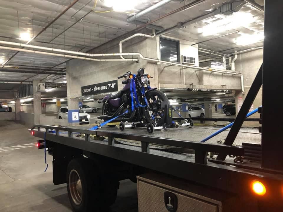 A motorcycle is being towed by a tow truck in a parking garage.