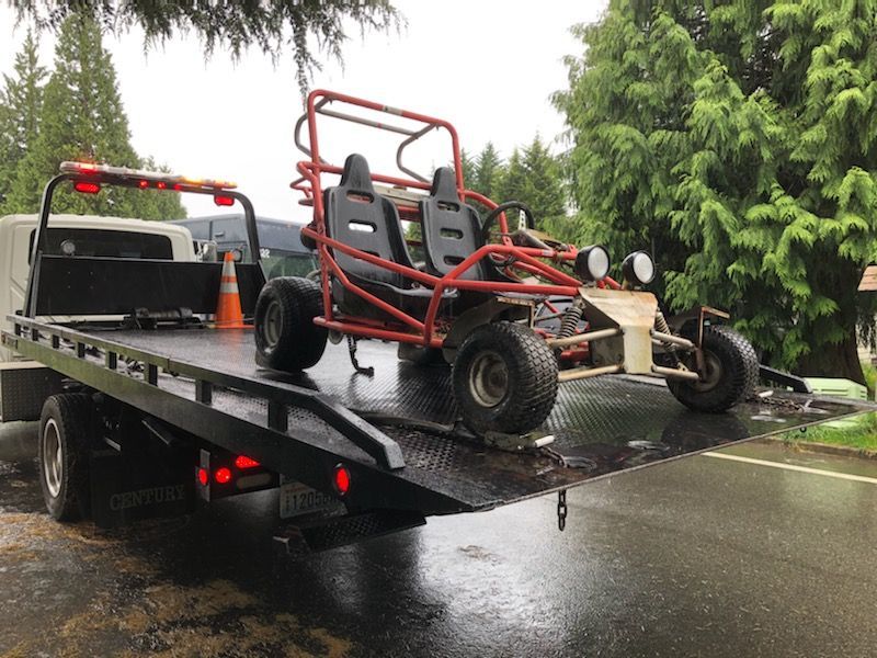 A tow truck is carrying a buggy on the back of it.