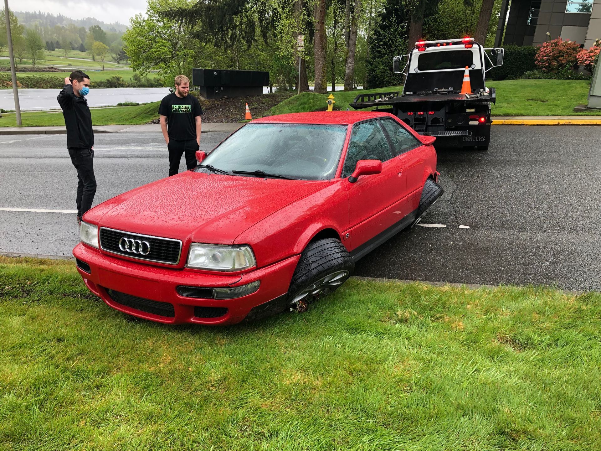 A red car with a flat tire is being towed by a tow truck.