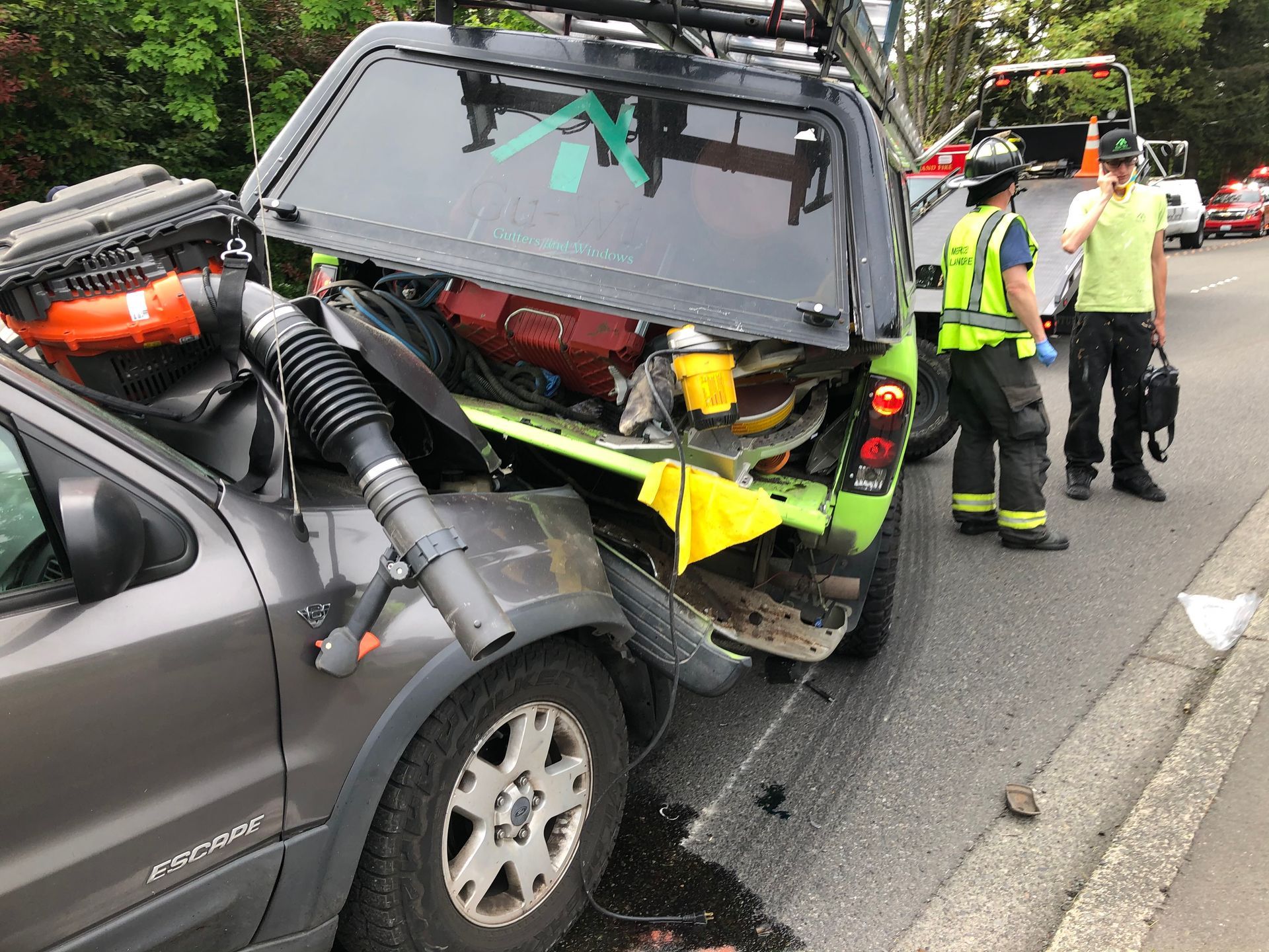 A man in a yellow vest is standing next to a car that has crashed into another car.