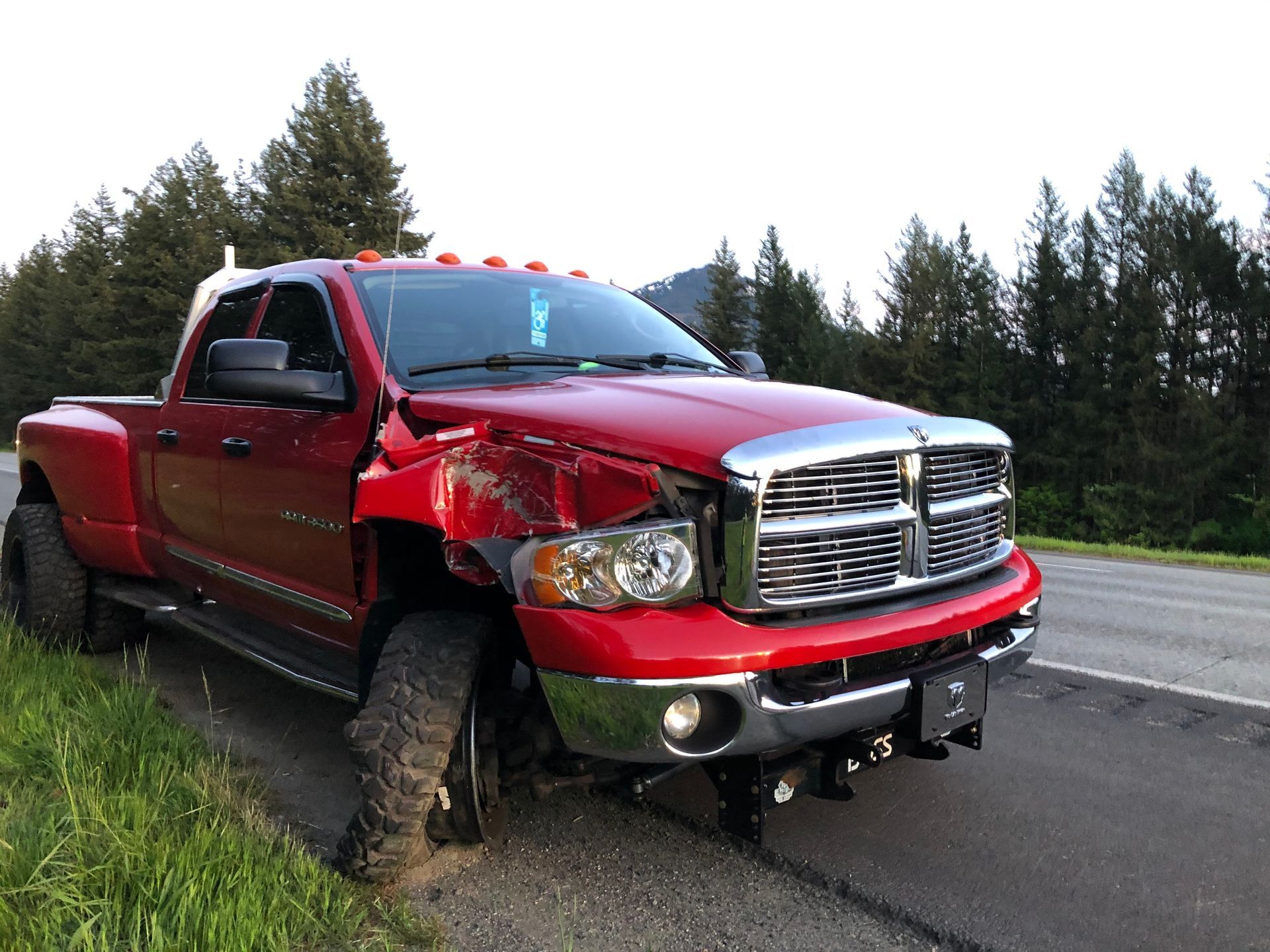 A red truck with a damaged front end is parked on the side of the road.