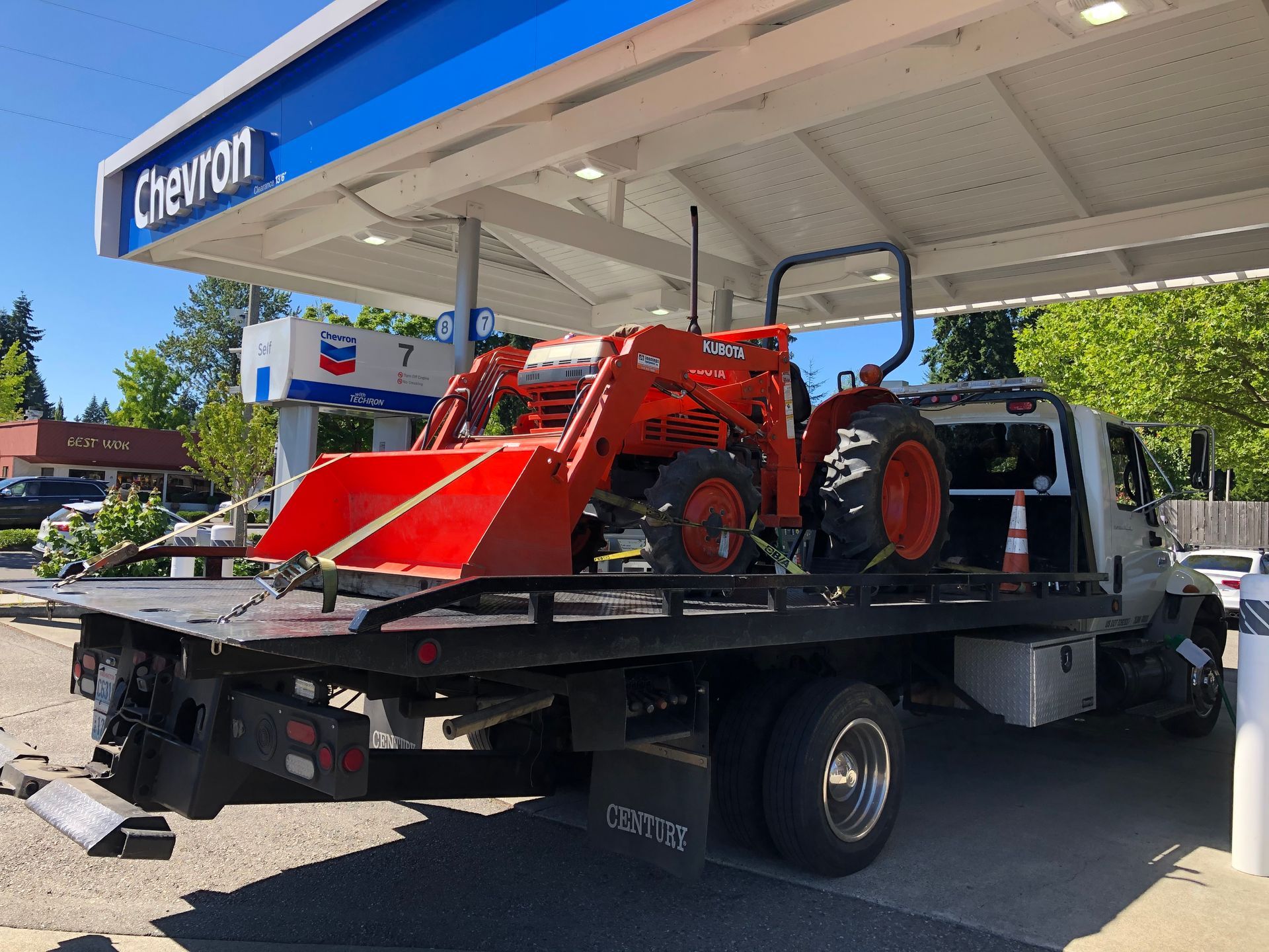 A tow truck with a tractor on the back is parked in front of a chevron gas station.