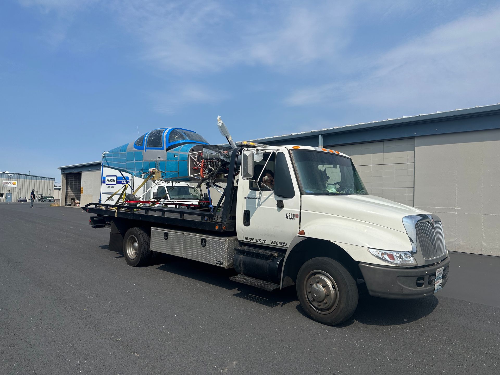 A white tow truck is carrying a blue airplane on the back.