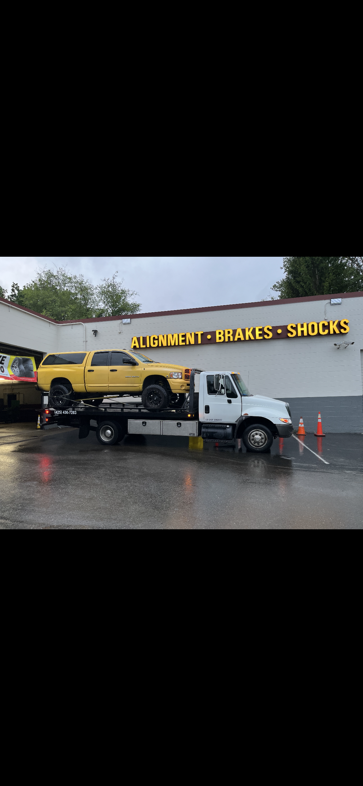 A yellow truck is being towed by a tow truck in front of a building.