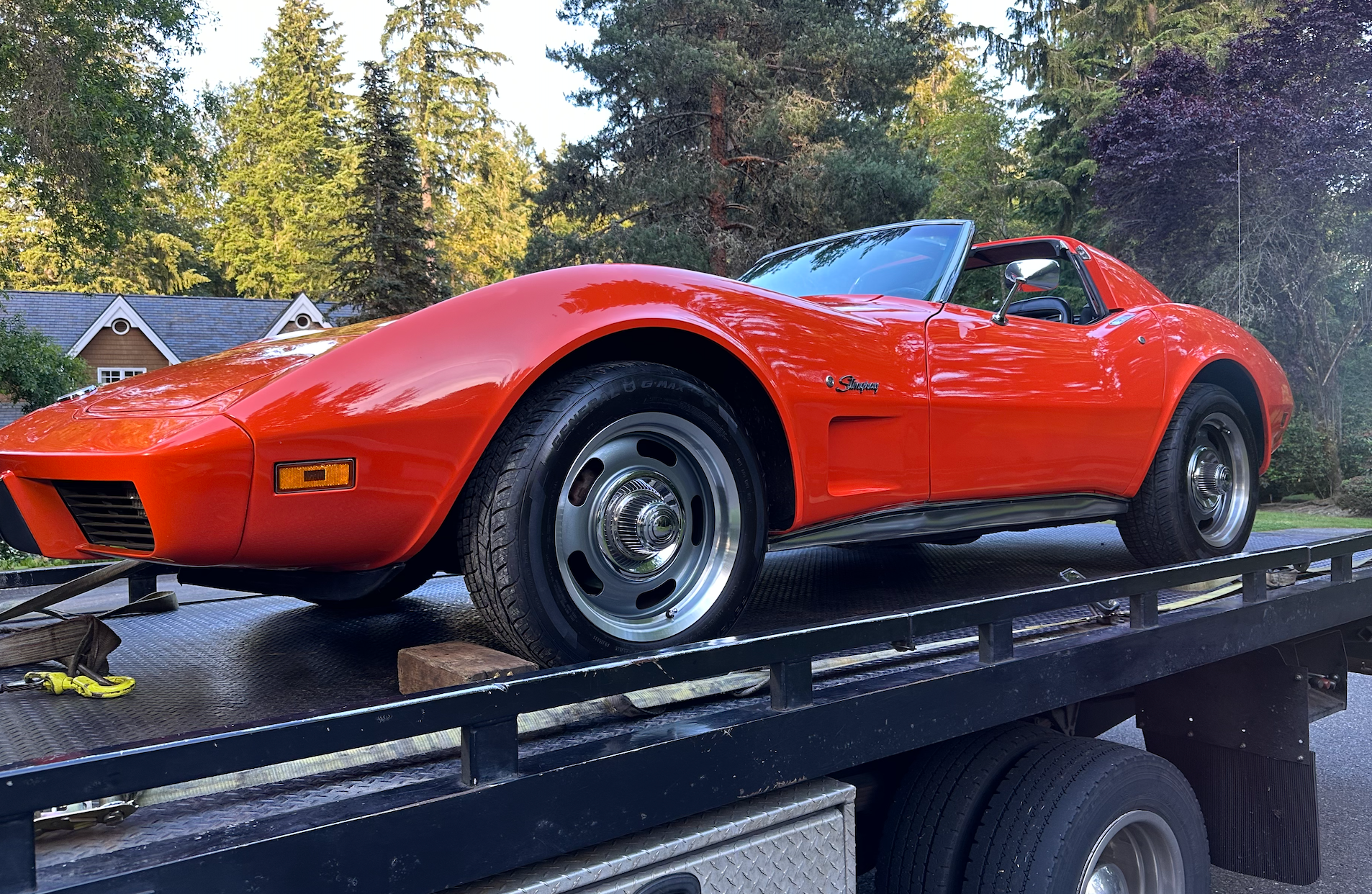 A red corvette is sitting on top of a tow truck.