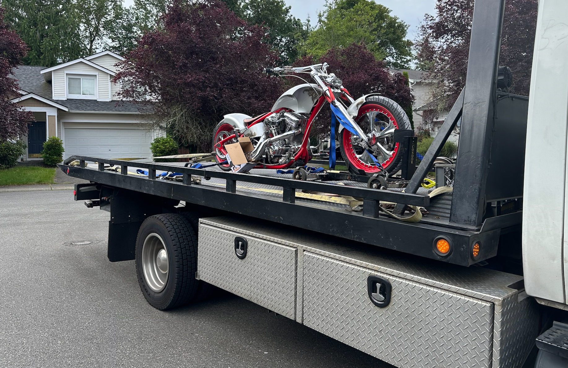 A tow truck with two motorcycles on the back is parked in front of a house.