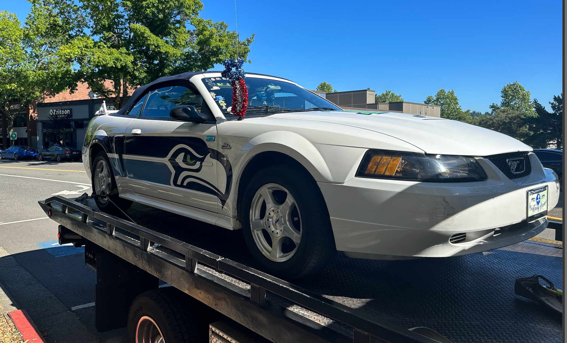 A white convertible mustang is sitting on top of a tow truck.