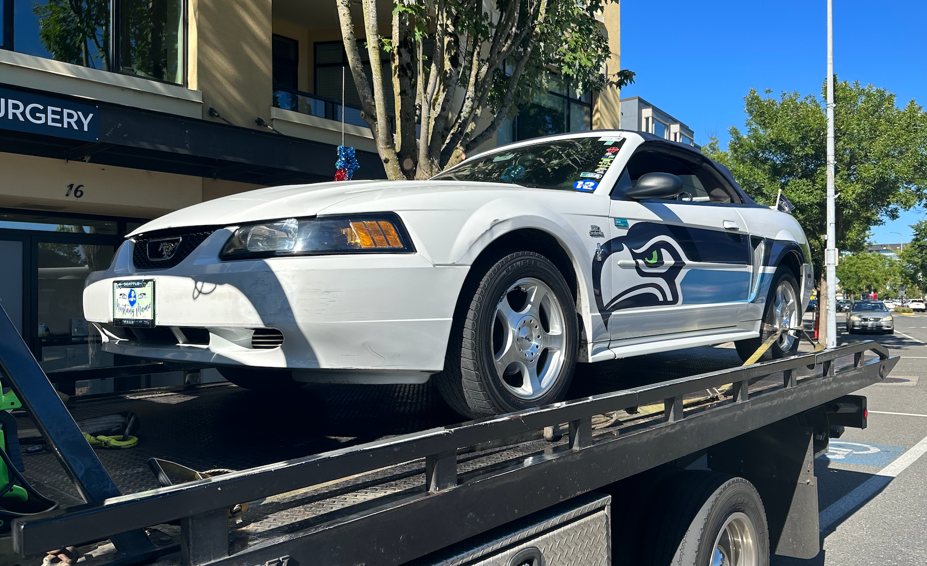 A white mustang is sitting on top of a tow truck.