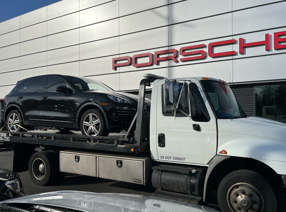 A tow truck is carrying a black porsche on the back of it.