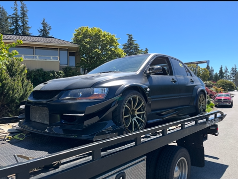 A black car is sitting on top of a tow truck.