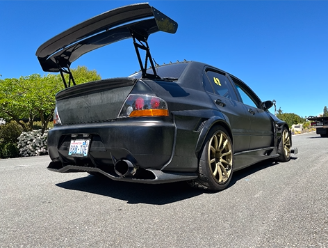 A black car with a spoiler on the back is parked in a parking lot.