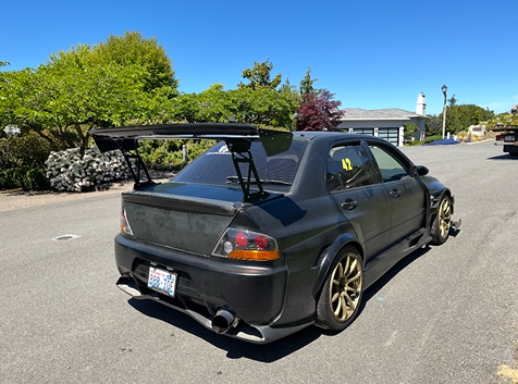A black car with a spoiler is parked in a parking lot