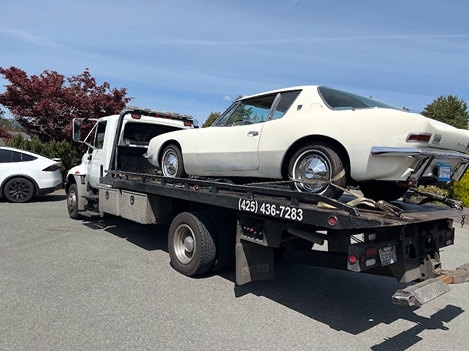 A white car is being towed by a tow truck.