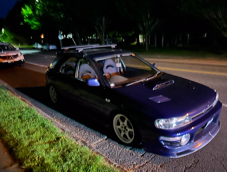 A purple car is parked on the side of the road at night