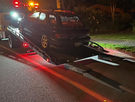 A car is being towed by a tow truck at night.
