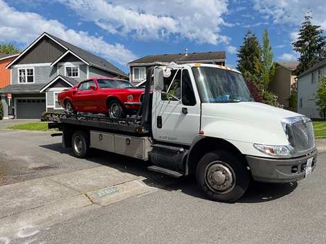 A tow truck with a red car on the back is parked in front of a house.