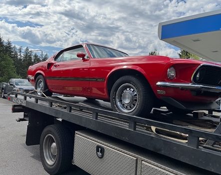 A red mustang is being towed by a tow truck.