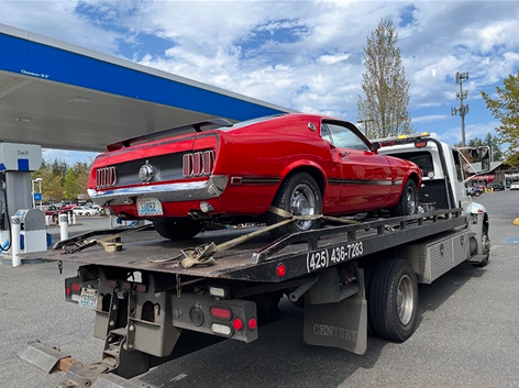 A red mustang is being towed by a tow truck.