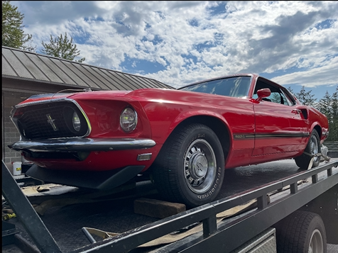A red mustang is sitting on top of a tow truck.