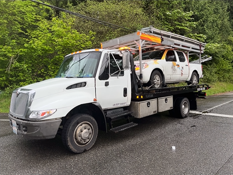 A tow truck with two cars on the back is parked on the side of the road.